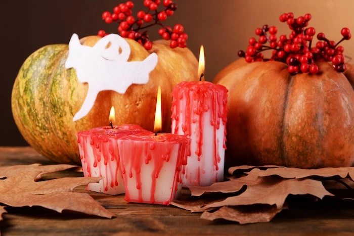 Halloween-Kerzen mit Blut-Optik, dahinter Kürbisse, ein Geist aus Papier und Herbstlaub.