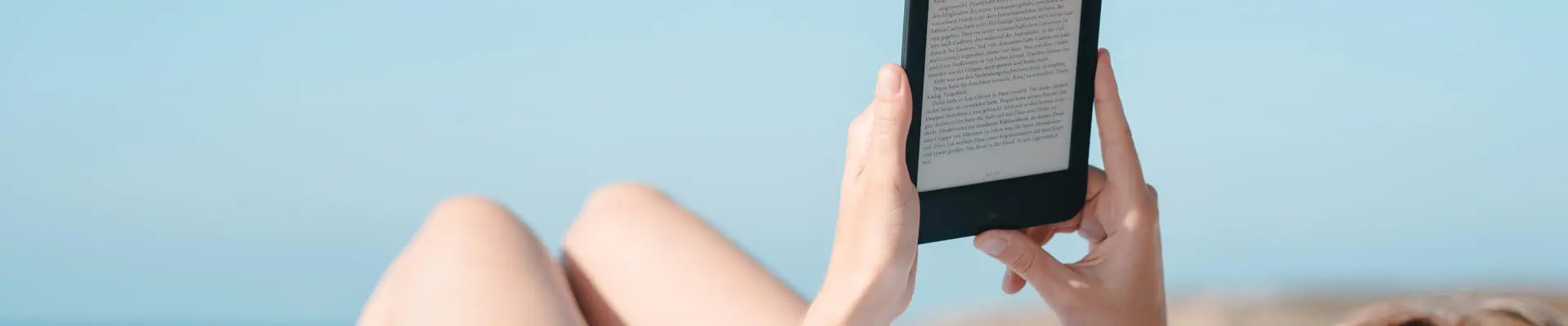 Schmuckbild: Frau liegt am Meer und hat E-Book-Reader in der Hand