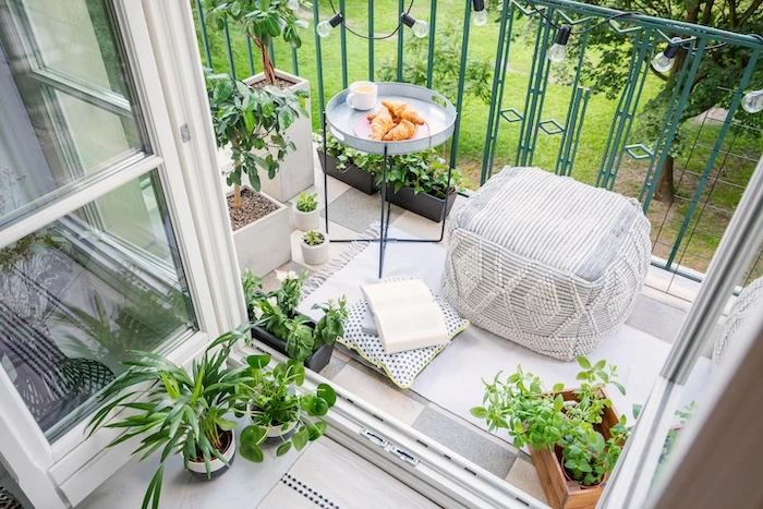 Schmuckbild: Kleiner Balkon mit grünem Geländer, einem Sitzsack, einem kleinen Beistelltisch mit Kaffee und Croissants, einem Buch und ringsherum Pflanzen wie Kräuter.