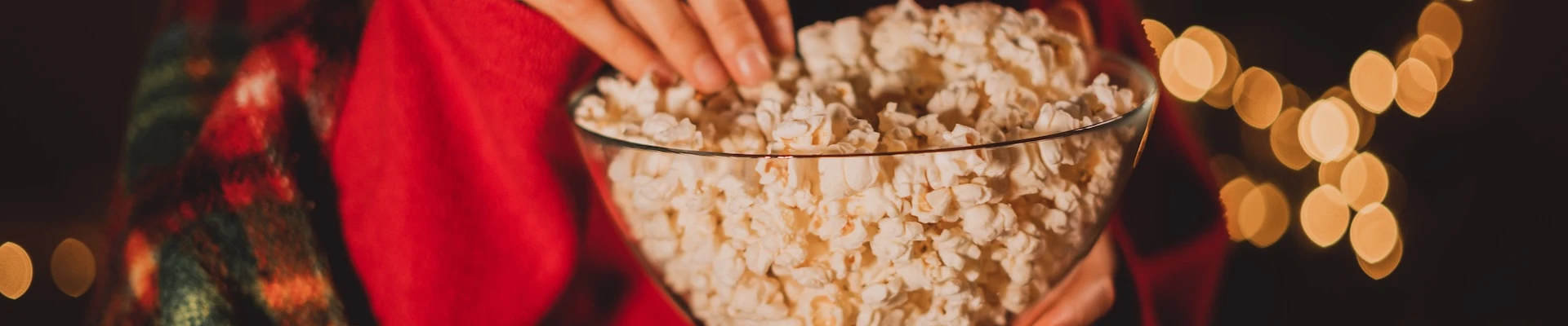 Schmuckbild: Frau, die Popcorn isst und einen roten Pullover trägt, im Hintergrund Lichterketten.