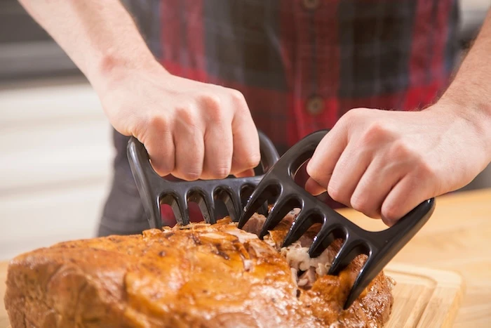 Schmuckbild: Mann, der mit Pulled Pork Krallen ein Stück Fleisch zerkleinert.