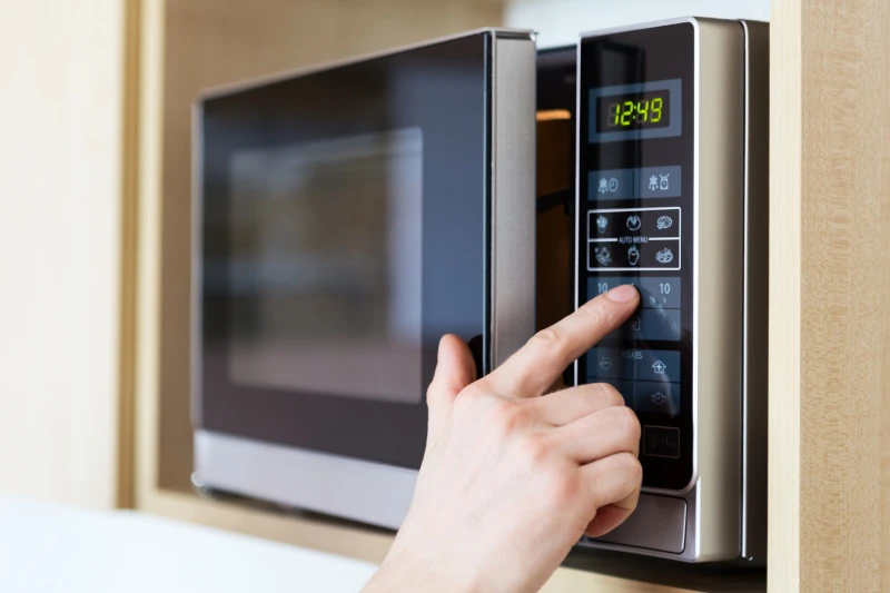 Schmuckbild: Eine Hand vor dem Touchpad einer Mikrowelle. Der Zeigefinger deutet auf ein Symbol.
