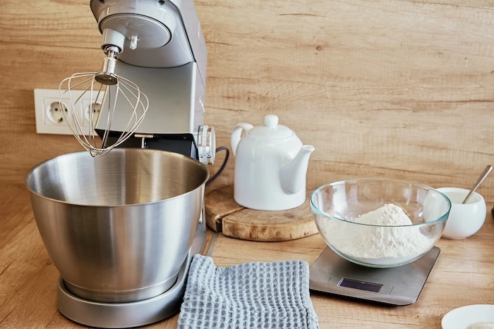 Küchenmaschine mit Knetaufsatz, daneben eine Küchenwaage und Schüsseln.