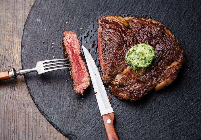 Schmuckbild: Ein Steak mit Kräuterbutter auf einer Schieferplatte, daneben Steakbesteck mit Steakmesser.