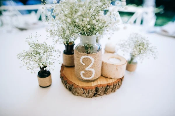 Schmuckbild: Holzscheibe mit Blumenvase und Platznummer darauf sowie Kerzenhalter aus Holz