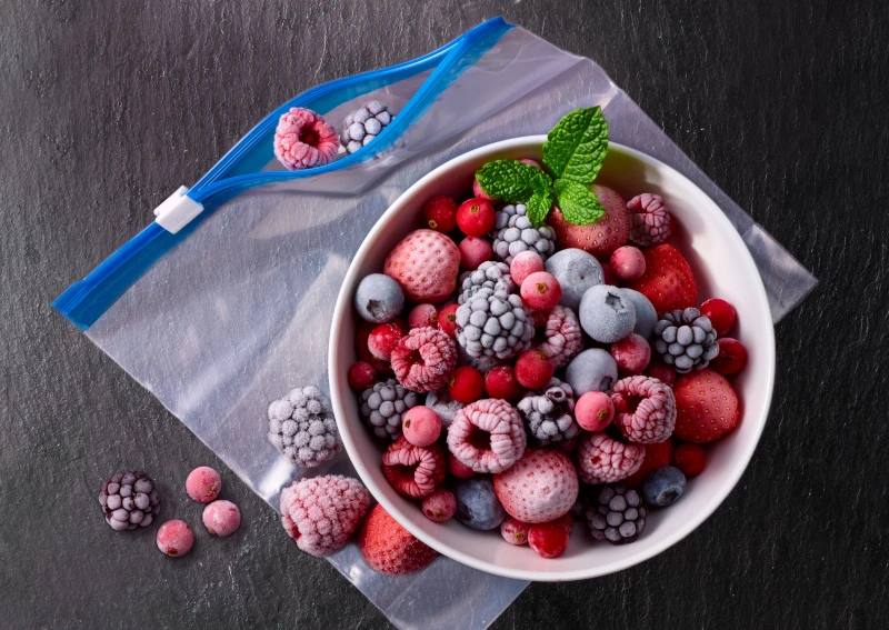 Schmuckbild: Gefrierbeutel, auf dem eine weiße Schale steht, die mit verschiedenen gefrorenen Beeren gefüllt ist.