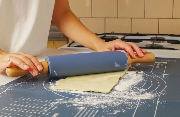 Frau rollt Teig auf Backmatte aus