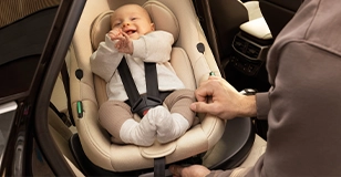 Werbung: Ein lachendes Baby sicher angeschnallt in einer hellen Kinderkraft Babyschale im Auto.