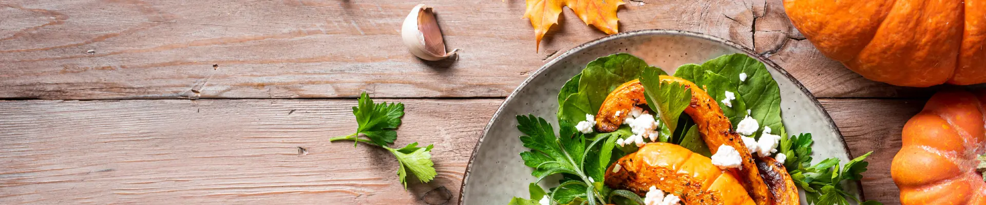 Schmuckbild: Ein Teller mit Kürbisstreifen und Salat, daneben Kürbisse, Ahornblätter und Knoblauch als Deko
