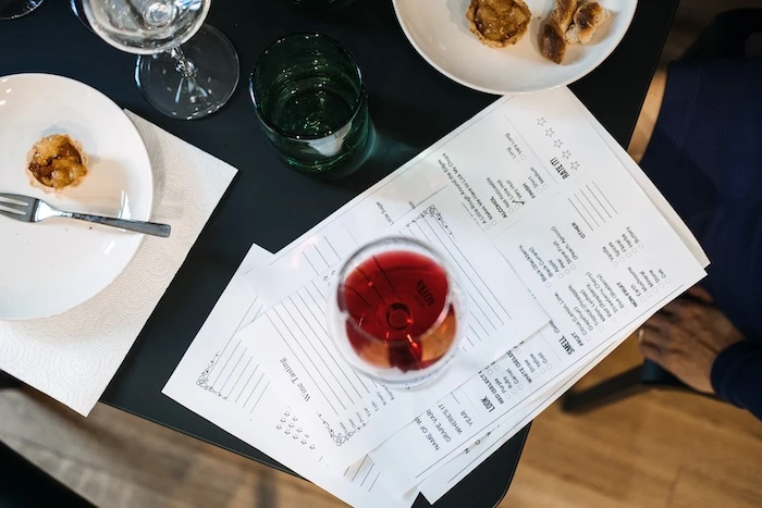 Schmuckbild: Ein Glas Rotwein, das auf Verkostungsbögen steht, daneben ein paar Teller und Gläser.