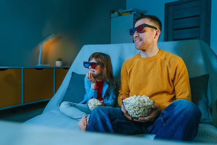 Schmuckbild: Ein Mann und ein Mädchen, die zusammen einen 3D-Film gucken und 3D-Brillen tragen, während sie Popcorn in der Hand halten.