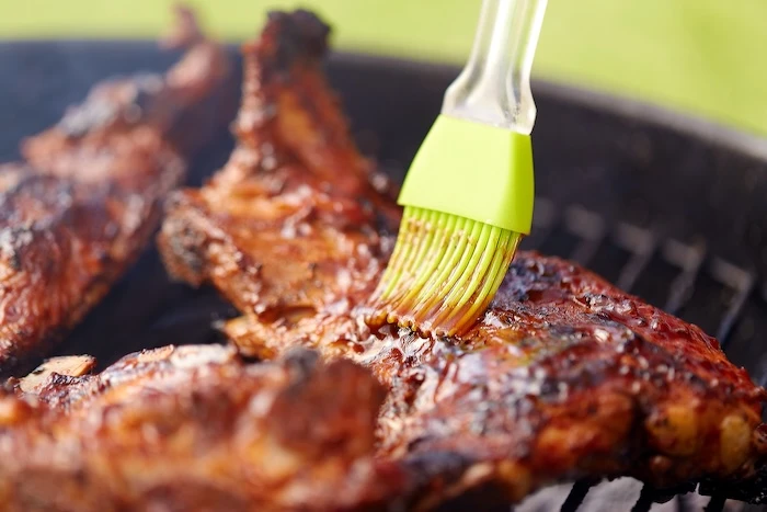 Schmuckbild: Fleisch, das auf einem Grill mit einem Silikonpinsel bestrichen wird.