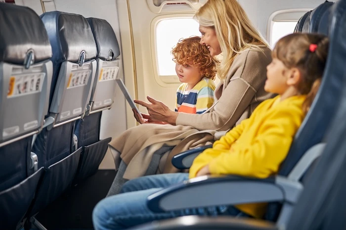 Schmuckbild: Eine Mutter mit zwei Kindern in einem Flugzeug, mit einem Tablet in der Hand.