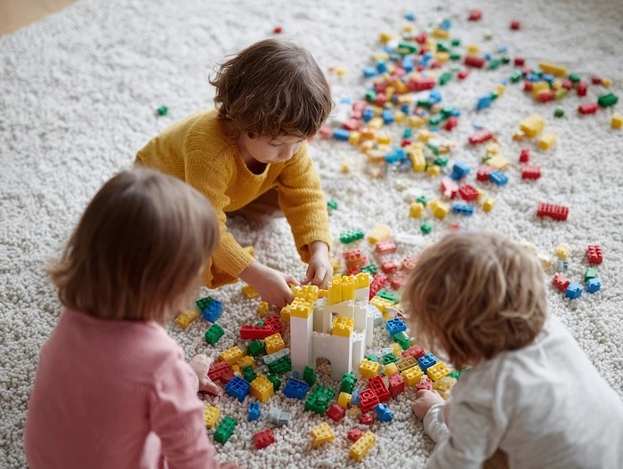 Kinder sitzen auf einem Teppich und spielen mit bunten Bauklötzen