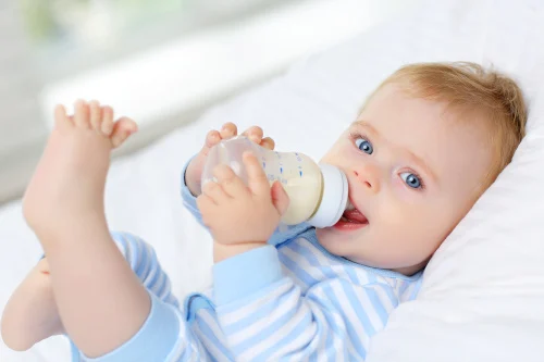 Schmuckbild: Säugling hält Babyflasche mit Milch in den Händen und saugt am Sauger.