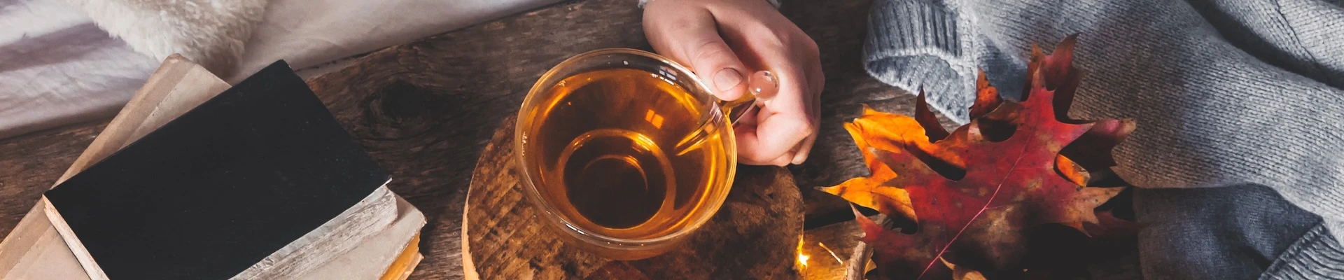 Schmuckbild: Tasse Tee, daneben Notizbücher, Herbstblätter und ein Pullover.