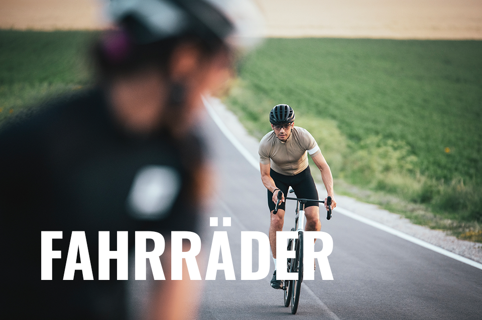 Werbung: Zwei Rennradfahrer auf einer Landstraße, umgeben von grünen Feldern. Text-Overlay im Vordergrund: Fahrräder.