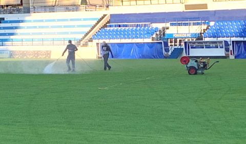 Δύο εργάτες συντηρούν ένα γήπεδο ποδοσφαίρου ψεκάζοντας το γρασίδι.