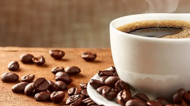 Frisch gebrühter Kaffee in einer Tasse mit Kaffeebohnen auf einem Tisch.
