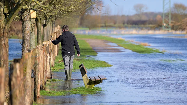 © dpa Ein Mann watet mit Gummistiefeln durch das Wasser. Noch sind viele Felder und Wiesen überschwemmt und nicht alle Straßen wieder trocken.