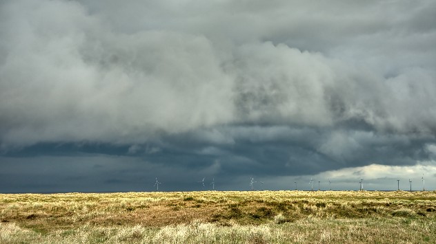 Stormy rainclouds pictured above wind turbines in an open field.