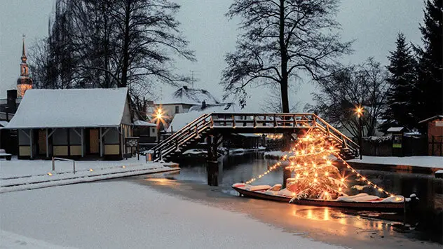 Kahn mit einem beleuchteten Weihnachtsmarkt auf einem Kanal im verschneiten Spreewald