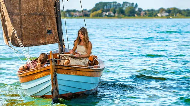 Carola Pieper sitzt in einem alten Boot und malt auf dem Bodden