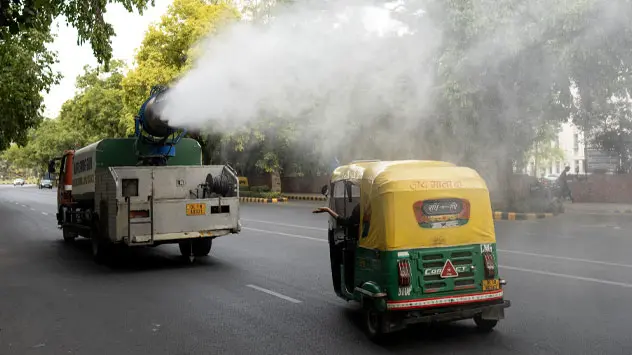 Een vrachtwagen van de gemeente sprenkelt water op een weg om het smelten van het asfalt tegen te gaan in New Delhi. 