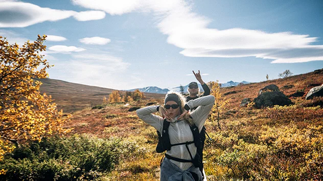 Zwei Personen in GORE-TEX Bekleidung wandern bei Sonnenschein durch eine herbstliche Berglandschaft.