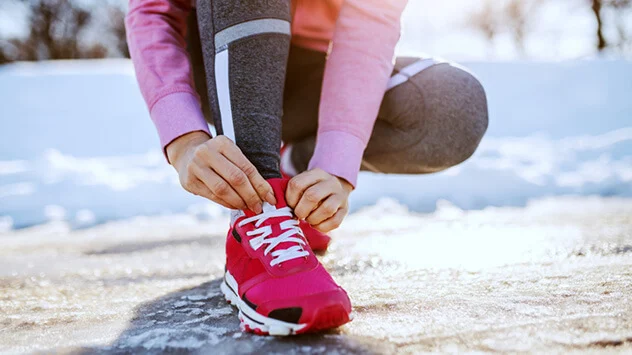 Frau schnürt sich den Schuh beim Laufen im Winter