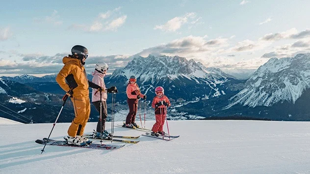 Eine Familie auf Skiern vor einer Bergkulisse. 