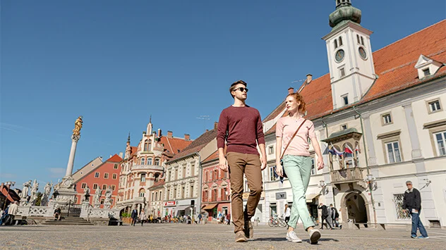 Mann und Frau spazieren über den Marktplatz von Maribor