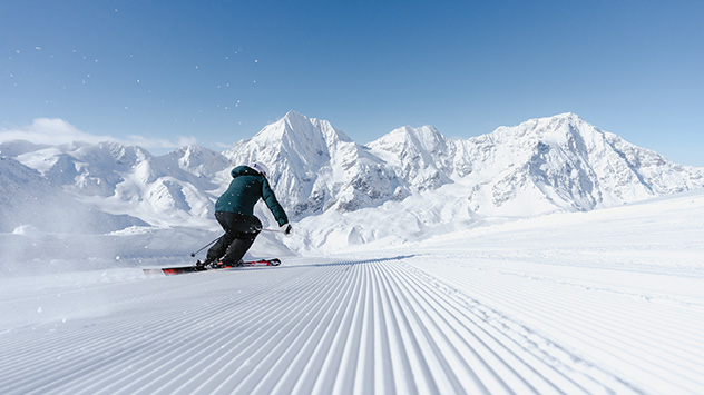 Skifahrer auf einer gut präparierten Piste, im Hintergrund die Alpen