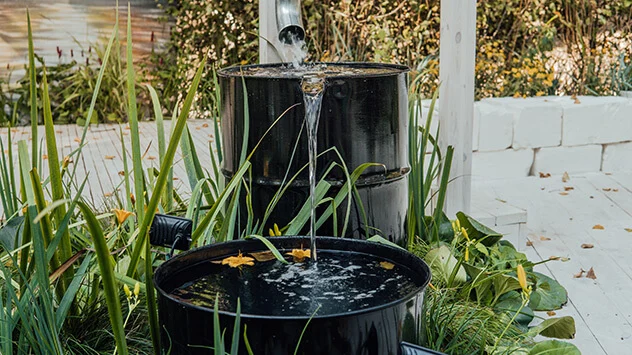 Wasser sparen beim Pflanzen gießen im Sommer Regenwasser fließt in Regentonne mit Überlauf