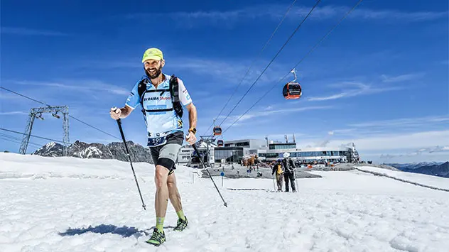 Laufteilnehmer mit Nordic-Walking-Stöcken nahe einer Bergstation im Schnee