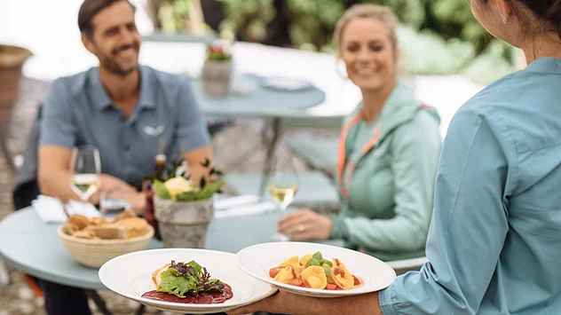 Gäste genießen regionale Speisen und Wein auf einer Terrasse im Freien. 