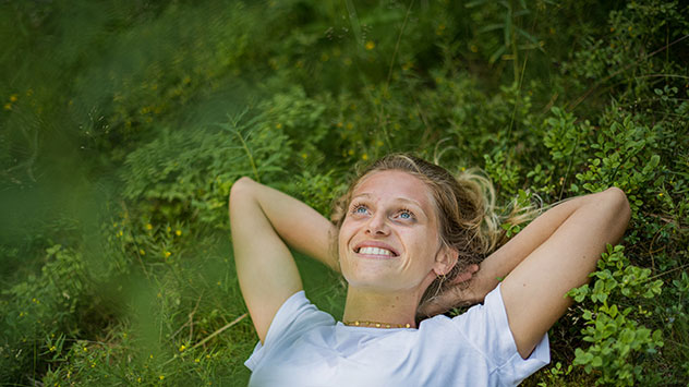 Eine Frau liegt auf einer Wiese und genießt Ruhe und frische Luft.