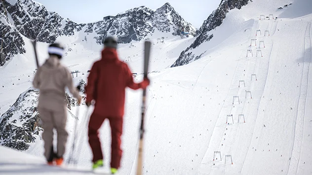 Winterulaub im Tiroler Stubaital - Bild: Sebastian Marko Zwei Skifahrer, die ihre Ski in den Händen halten, schauen in Richtung einer Skipiste.