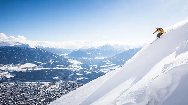 Skifahrer fährt steilen Hang herunter mit Blick auf Innsbruck im Tal.