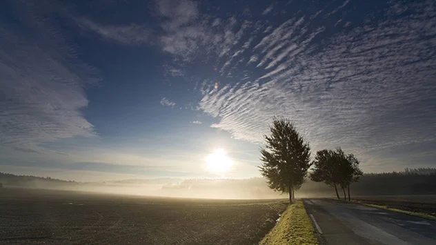 Schäfchenwolken in Rippelform über neblige Landschaft mit Sonnenaufgang