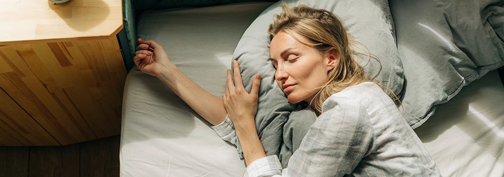 Eine Frau schläft entspannt in einem hellen Schlafzimmer. 
