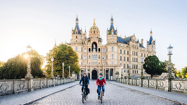 Ein radelndes Paar, im Hintergrund das Schweriner Schloss