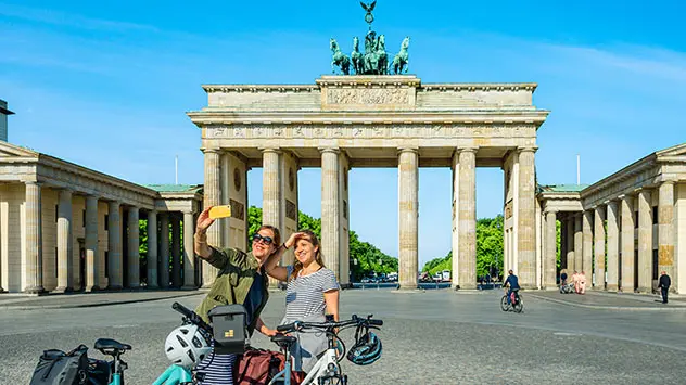 Zwei Frauen mit Fahrrädern machen ein Selfie vor dem Brandenburger Tor 