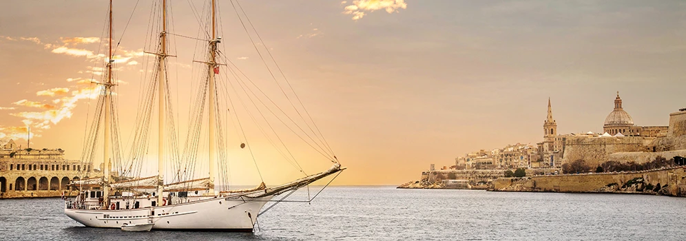 Segelboot vor der historischen Küste von Valletta auf Malta bei Sonnenuntergang, mit Blick auf die Altstadt.