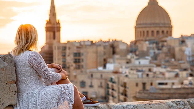 Eine Frau blickt bei Abendrot auf die Altstadt von Valletta. 