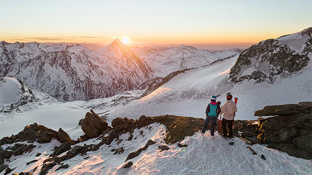 Ein Paar beobachtet auf einem Gipfel stehend den Sonnenaufgang in den Bergen