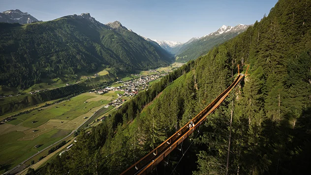 Wanderer auf der Hängebrücke des Sunnenseit’n Weges mit Panorama auf die Stubaier Alpen