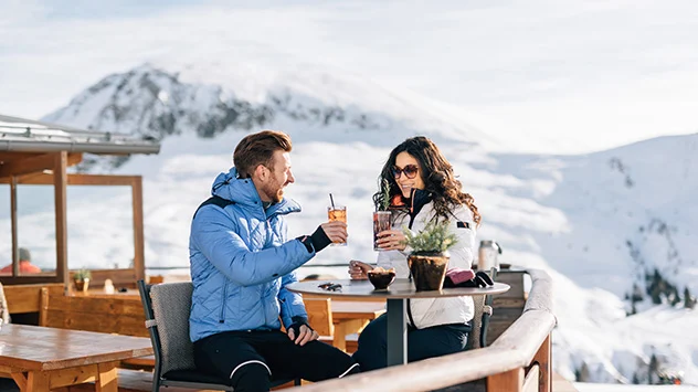 Ein Paar stößt auf einer Berghütte mit Getränken an. 