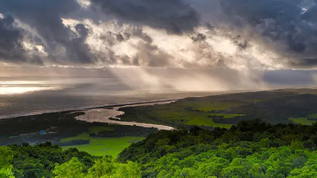 Grüne Landschaft mit Fluss und Wäldern am ruhigen Meer gelegen. Wolkiger Himmel