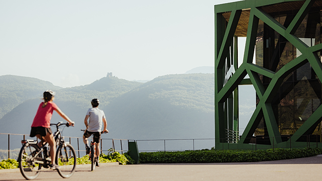 Radfahrer vor einer modernen Kellerei mit markanter Architektur und Blick auf die Weinlandschaft.